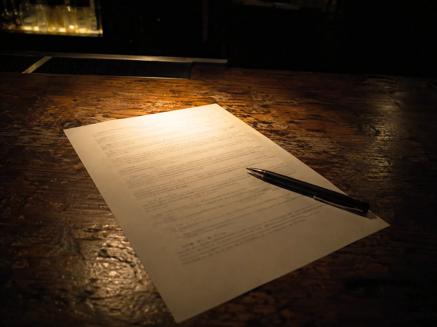 A printed artist agreement resting on a bar top with a pen